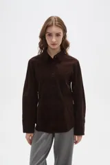 Camisa de pana color marrón, con cuello camisero, cierre frontal de botones y bolsillos en el pecho. Presenta un corte entallado y mangas largas.