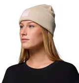 Gorro tipo beanie de tejido grueso color beige, con diseño de punto acanalado y vuelta en el borde. Presenta un parche cuadrado en el frente con el logo de la marca Columbia.