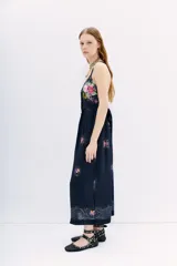 Vestido midi de viscosa con estampado floral sobre fondo azul oscuro. Presenta escote delantero, breteles finos que se cruzan en la espalda y cintura con lazo ajustable.