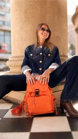 Mochila de nylon color naranja, con tapa superior y cierre de broche, bolsillo frontal con cierre y bolsillos laterales. Incluye correas regulables para la espalda y asa de mano.