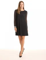 Vestido negro de seda fría con silueta evasé, cuello redondo y mangas largas de gasa transparente. Los puños son anchos y están decorados con una densa aplicación de perlas blancas.