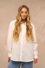 Camisa blanca oversize de manga larga, con cuello camisero, cierre frontal de botones y diseño bordado con motivos marinos perforados.