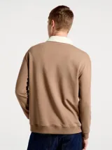 Buzo de estilo polo con cuello camisero en color crema y cuerpo en tono marrón. Presenta cierre frontal con botones, mangas largas y puños acanalados.
