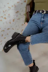 Botas tipo chelsea de caña corta, confeccionadas en cuero con textura de reptil en color negro. Presentan punta cuadrada con puntera metálica decorativa, elásticos laterales para un calce sencillo y taco cuadrado bajo.