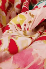 Vestido largo con estampado caleidoscópico en tonos rosa, rojo y verde. Presenta tirantes finos, escote en V, corte imperio y falda con volantes. Incluye detalle de trenzas en el pecho y la cintura que se anudan en la espalda descubierta.