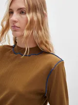 Polera de manga larga confeccionada en tela rib color bordó, con cuello alto y hombreras. Presenta costuras a la vista con pespuntes en hilo de color contrastante en el cuello, puños, hombros y ruedo.