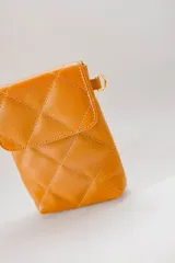 Cartera mini color mostaza de cuero capitoneado, con correa regulable para colgar al hombro.