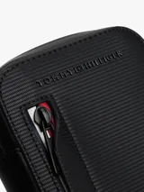 Cartera cruzada para teléfono de Tommy Hilfiger, color negro, con diseño compacto y funcional. Presenta un bolsillo frontal con cierre y detalles distintivos de la marca en los colores icónicos, además del logo metálico en la parte superior.