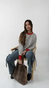 Sweater de punto con diseño a rayas horizontales en blanco y negro, cuello redondo y puños en color rojo vibrante. Presenta un calce relajado y holgado.