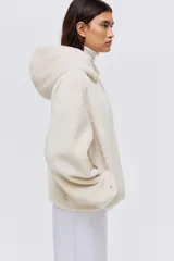 Campera de tejido suave con efecto de piel sintética, corte holgado y hombros caídos. Presenta capucha forrada, cierre frontal con cremallera y bolsillos laterales ocultos en las costuras.