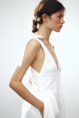 Vestido midi blanco de algodón, con escote pico pronunciado y tirantes anchos ajustables con lazada. Presenta elástico en la cintura y falda con pliegues.