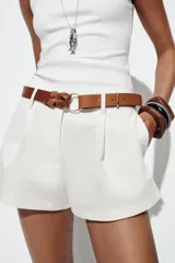 Bermuda blanca de tiro alto con pliegues frontales y bajo ancho. Incluye un cinturón trenzado de cuero marrón con hebilla redonda metálica.