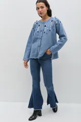 Saco de punto color rosa, con cuello redondo, cierre frontal con botones forrados en crochet y mangas largas. Presenta un delicado bordado floral artesanal que cae desde los hombros y detalles de calados en los puños y el ruedo.