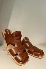 Zuecos negros de cuero charol con diseño de tiras entrecruzadas y suela plana.