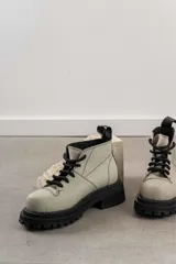 Botas de cuero color beige con suela track negra de goma y cordones gruesos negros. Presentan un diseño de caña baja con costuras visibles y puntera reforzada.