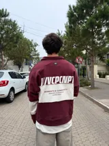 Buzo tipo polo de corte relajado y fit boxy, con diseño de bloques de color en bordó y blanco. Presenta cuello camisero con cierre frontal parcial y logo bordado en el pecho.