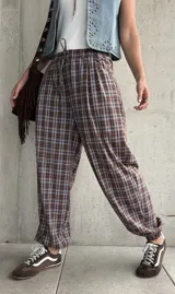 Pantalón babucha de corte holgado, con estampa de cuadros en tonos marrón y celeste, cintura elástica con cordón ajustable y puños fruncidos en los tobillos.
