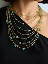 Collar de múltiples capas compuesto por hileras de cuentas tubulares doradas intercaladas con pequeñas piedras naturales en tono turquesa. Incluye cadena de extensión para regular el largo.