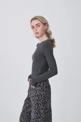 Remera de manga larga confeccionada en viscosa, con diseño entallado y cuello redondo a la base. Presenta una textura acanalada y terminaciones con ondas en los puños y el ruedo.