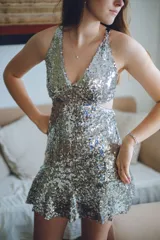 Vestido corto negro con estampado de plumas doradas, escote en V, breteles finos cruzados en la espalda, cut-outs laterales y volado en el ruedo.