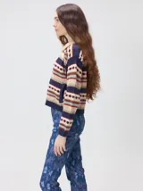 Campera de punto estampada de corte holgado, con cierre metálico frontal y cuello de corderito sintético en color tostado. Presenta un diseño de franjas horizontales con patrones geométricos en tonos bordó, mostaza, marrón y beige.