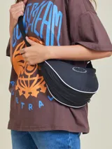 Bandolera negra de diseño curvo y estilo deportivo, con ribete blanco en el borde y logo de la marca en la parte frontal. Cuenta con correa ajustable y cierre superior.