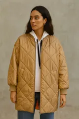 Campera larga color camel con diseño acolchado de rombos, cuello redondo y cierre frontal con cremallera.