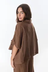 Camisa color beige de lino con cuello camisero, manga corta y cierre frontal con botones. Presenta detalles de encaje en el cuello, el frente y las mangas.