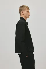 Campera negra de nylon levemente acolchada, con cuello y cierre frontal plateado. Presenta bolsillos insertados al bies y un bolsillo interior con botón a presión. Posee cordón elástico ajustable en el bajo.