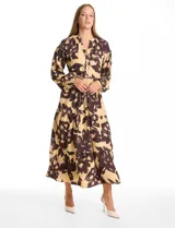 Vestido maxi de crepe con estampado floral en tonos beige y marrón oscuro. Presenta escote en V con botones frontales, mangas largas amplias con puños abotonados y cintura ajustable mediante cordón trenzado. La falda cuenta con un diseño de vuelos escalonados que aporta movimiento.