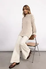 Sweater de tejido de punto con diseño de trenzas verticales, cuello alto, manga larga y silueta oversize de largo extendido.