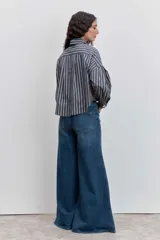 Camisa de corte oversize con diseño de rayas verticales en tonos azul y blanco, cuello clásico, cierre frontal con botones y mangas largas con puños abotonados.