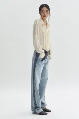 Jean de corte holgado y pierna recta confeccionado en denim de algodón rígido. Presenta un diseño bicolor con paneles en tonos contrastantes, costura desflecada en la cintura y franjas laterales. Cuenta con diseño de cinco bolsillos, cierre con botón y tachas metálicas con logo grabado.