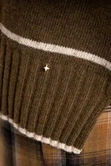 Sweater de lana con diseño de rayas horizontales blancas sobre fondo verde oliva. Presenta cuello redondo, mangas largas con puños acanalados y un corte oversize con tajos laterales en el ruedo.