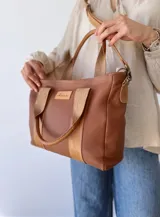 Bolso tipo tote de cuero color marrón con doble asa corta y correa larga extraíble.