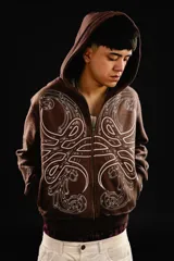 Hoodie con cierre frontal, color marrón, con diseño estampado de hojas de acanto en color blanco que recorre el frente y las mangas. Cuenta con bolsillos laterales y costuras visibles.