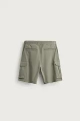 Bermuda cargo color negro de corte relaxed fit, confeccionada en tejido de algodón con elasticidad y efecto lavado. Cuenta con cintura elástica ajustable con cordón, bolsillos frontales y bolsillos laterales tipo cargo con solapa en las perneras.