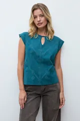 Remera de manga corta color verde petróleo, con cuello redondo y detalle de abertura tipo gota en el frente. Presenta un diseño con bordados geométricos tono sobre tono en la parte frontal.