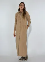Vestido largo tipo camisero color beige, con botones frontales, cuello camisero, mangas largas con puños abotonados y bolsillos en el pecho.