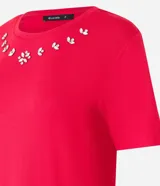 Remera de viscosa color rojo, corte clásico, con cuello redondo y mangas cortas. Presenta aplicación de strass en el escote.