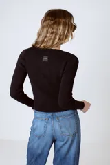 Top negro de tejido de punto acanalado con mangas largas y cierre frontal con botones decorativos.