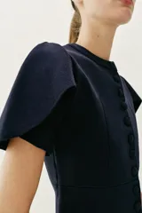 Chaqueta entallada azul marino de punto, con cuello redondo y mangas cortas abullonadas con aberturas. Cierre frontal con botones forrados a tono.