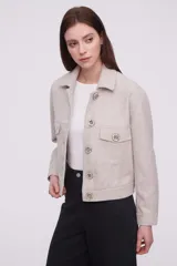 Chaqueta corta color arena melange con cuello camisero, cierre frontal con botones dorados y bolsillos de parche en el pecho.