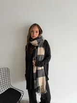 Bufanda de tejido suave con diseño de cuadros grandes en tonos negro y beige, terminada con flecos en los extremos.