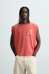 Camiseta tank cropped fit color ladrillo, con cuello redondo y sisa. Estampado frontal y trasero con gráficos y textos en color amarillo. Efecto lavado.