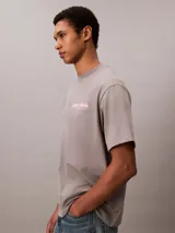 Remera gris de corte regular y mangas cortas, con cuello redondo y el logotipo de Calvin Klein bordado en color rosado en el pecho.