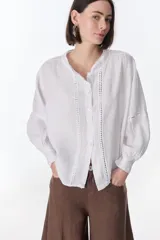 Camisa blanca de lino con cuello mao, mangas largas abullonadas y detalles de puntilla en el frente y los hombros.
