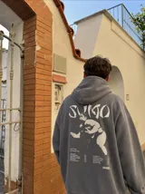 Canguro con capucha gris oscuro, con bolsillo tipo canguro y estampa frontal blanca con texto.