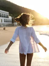 Camisa blanca de lino con cuello clásico, mangas largas y cierre frontal con botones color madera. Presenta detalles de frunces verticales en el frente.