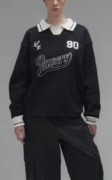 Sweater de punto negro con cuello polo en color crema, manga larga y diseño oversize. Presenta bordados en el frente con la inscripción 'Ravers', el número '90' y letras cursivas, con terminaciones en punto rib en puños y cuello.